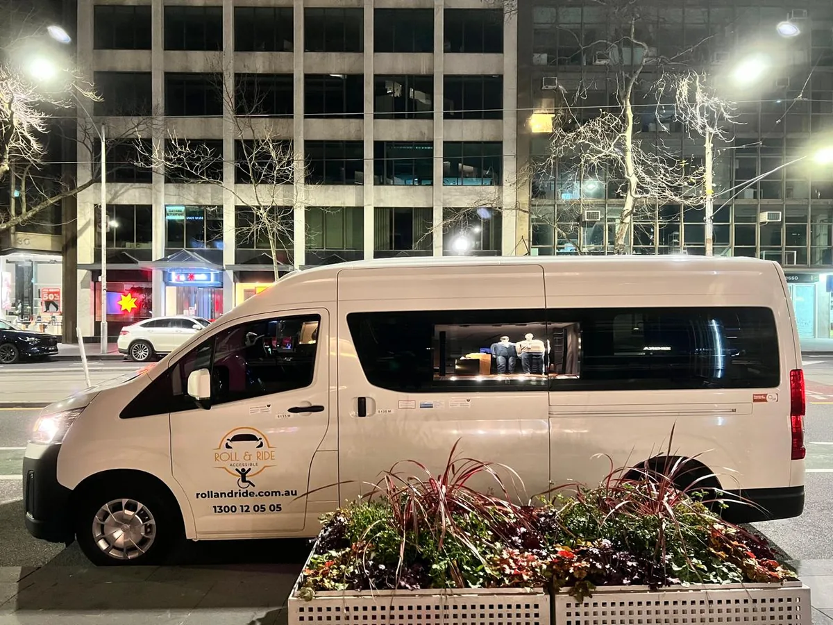 A Roll & Ride wheelchair accessible van parked on a Melbourne city street at night, showing rollandride.com.au and 1300 12 05 05 on the door.