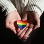Close-up of hands cradling a rainbow heart, symbolizing love and LGBTQ+ pride.